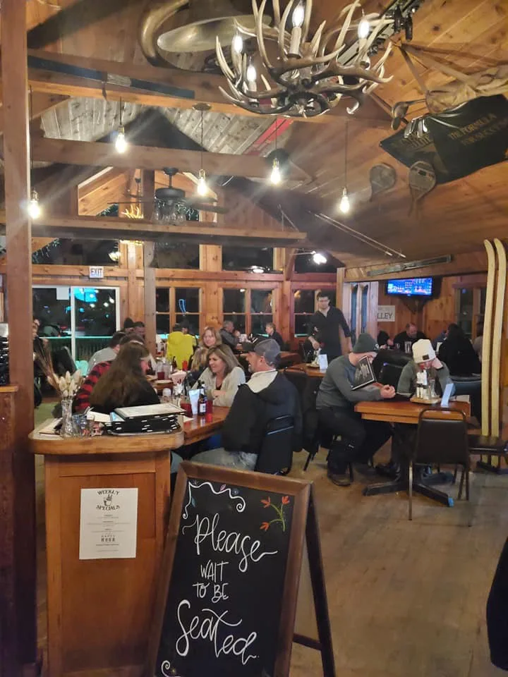 Busy lodge dining room with an antler chandelier and a Please wait to be seated chalkboard