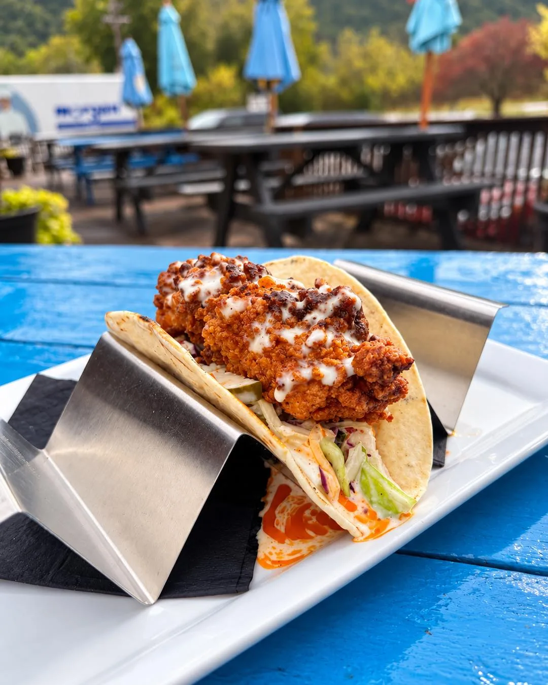 Nashville hot chicken taco on a blue patio table, umbrellas and wooded hills behind