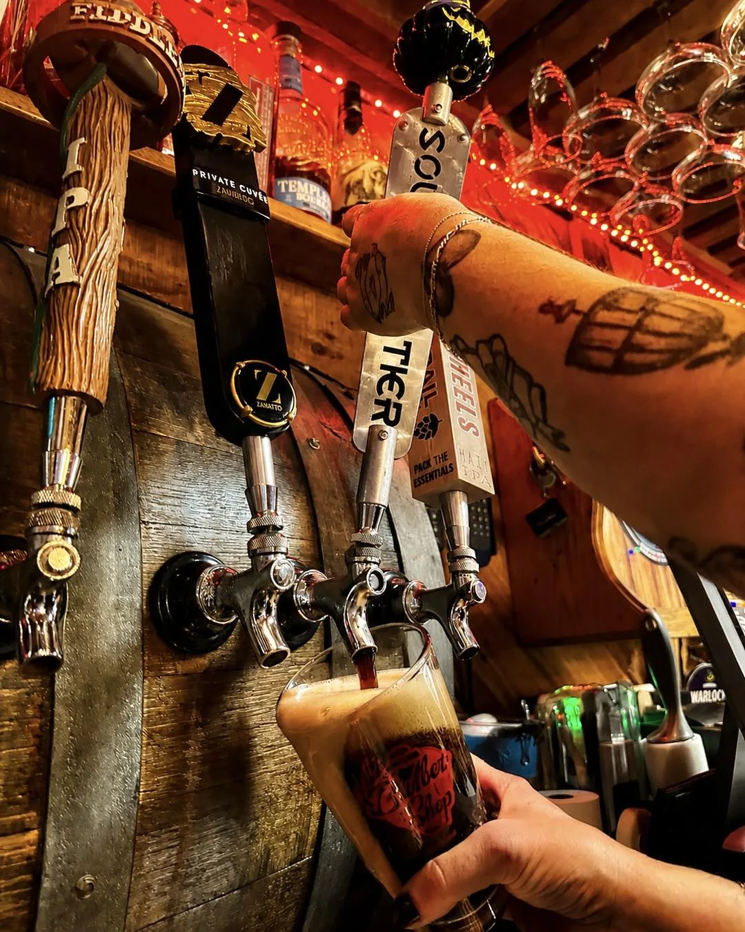 Bartender pouring a dark beer from tap handles set in a wooden barrel